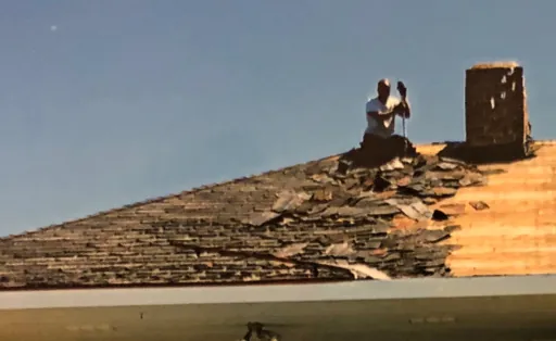 Before: roofer tearing off old shingles near the museum chimney