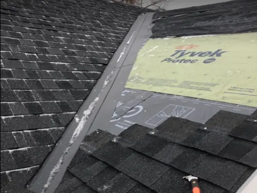 Shingle repair along a roof valley with a hammer on the roof